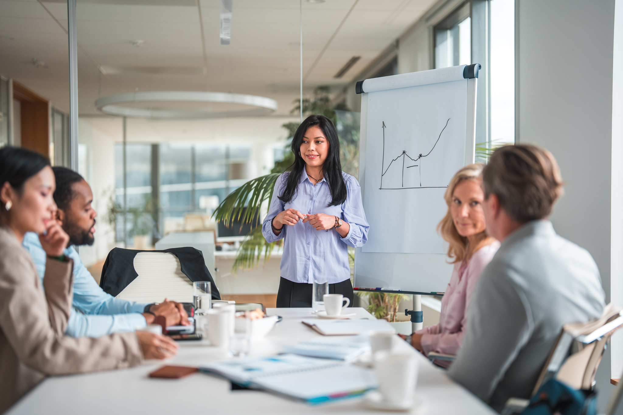 Latina Woman Standing in Conference Room With Board Members Sitting